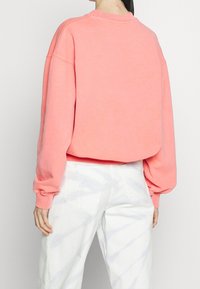 Koraalroze sweatshirt met een ronde halslijn en verlaagde schouders, voorzien van geribbelde manchetten en een relaxte pasvorm, gecombineerd met witte tie-dye jeans.