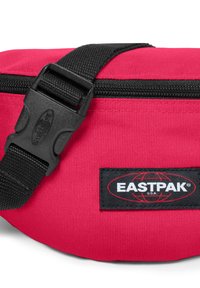 Marsupio in tessuto rosso con chiusura zip nera, cinturino regolabile e etichetta EASTPAK in bianco e nero. Materiale resistente, design compatto.