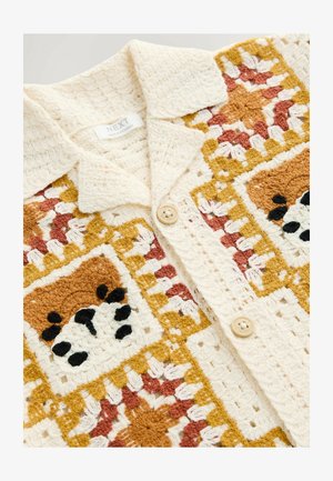 Krém, sárga, rozsdabarna és fekete színű, horgolt gombos dzseki. Texturált négyzetmintákkal és galléros nyakkal rendelkezik, gombokkal ellátva.