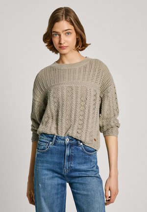 Lichtgrijze gebreide trui met een textuurpatroon, ronde halslijn en driekwartmouwen, gecombineerd met blauwe high-waisted jeans.