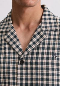Camicia a quadri blu navy e panna con colletto, chiusura con bottoni e ricamo sottile sul petto, realizzata in tessuto strutturato.