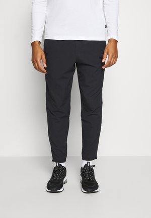 Czarne lekkie spodnie o zwężanym kroju, z suwakami przy kostkach i bocznymi kieszeniami, w połączeniu z czarnymi butami sportowymi i białymi skarpetami do kostek.