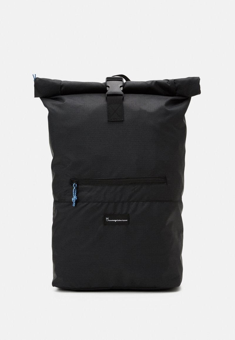 Sac à dos noir à fermeture roulante, poche avant zippée, tirette bleue et fermeture à boucle sur un fond uni clair.