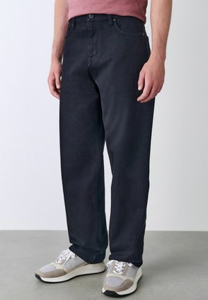 Dunkelblaue Straight-Leg-Jeans verfügen über ein klassisches Fünf-Taschen-Design, dezente Nähte und eine glatte Textur. Tragen mit grauen Sportschuhen.