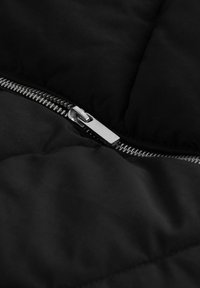 Czarny wyściełany materiał z teksturowanym przeszyciem, wyposażony w srebrny metalowy zamek błyskawiczny wzdłuż jednego brzegu oraz gładkie, matowe wykończenie.