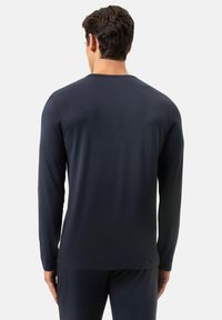 Granatowa koszula z długim rękawem, pokazana od tyłu. Wykonana z gładkiego materiału, z okrągłym dekoltem i minimalnymi przeszyciami. Klasyczny krój.