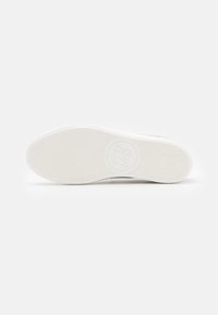 Suola di sneaker in gomma bianca con una superficie texturizzata, caratterizzata da un logo circolare e motivi di grip ottimali per la trazione.