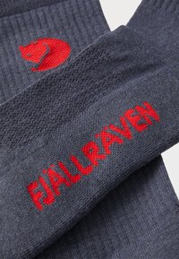 Mörkblå stickade strumpor med ett texturerat mönster. Röd logotyp och varumärkesnamn "FJÄLLRÄVEN" tydligt framhävt. Mjukt och elastiskt material.