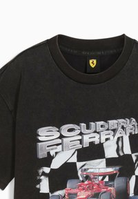 Schwarzes Baumwoll-T-Shirt mit Rundhalsausschnitt, das "SCUDERIA FERRARI" in fetten silbernen Buchstaben zeigt, sowie ein rotes Rennwagen-Graphic auf einem karierten Hintergrund.