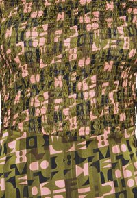 Patroon jurk met een donker groene, roze en zwarte abstracte print. Het bovenstuk heeft een geschrokken textuur, terwijl de rok geometrische ontwerpen toont.