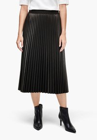 Falda midi plisada negra hecha de material sintético brillante, con una cintura alta. Combinada con botas de tobillo negras de punta.