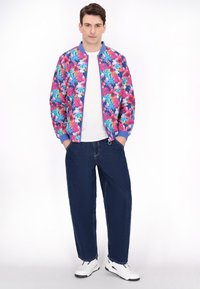 Jachetă bomber florală în nuanțe de roz, albastru și verde, cu manșete și talie ribbate. Purtați peste un tricou alb și asortați cu blugi de culoare albastră închis și adidași.