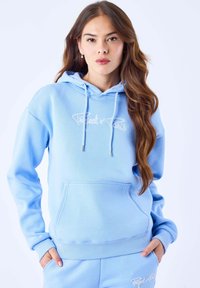 Sweat à capuche bleu clair en tissu doux, doté d'une poche kangourou, de poignets côtelés et d'un logo brodé en blanc sur le devant.