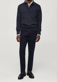 Maglione navy con colletto e tre bottoni, abbinato a pantaloni navy slim-fit e scarpe nere lucide. Texture liscia e design moderno.