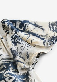 Tissu avec un motif abstrait de traits de pinceau bleu marine et beige, présenté en gros plan sur une section pliée avec une texture visible.