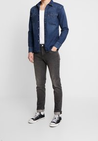 Mörkblå denimskjorta, knäppt med två bröstfickor. Matchad med grå jeans och svarta sneakers med vita sulor. Vit T-shirt under.