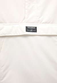 Hvid polstret stof med et sort Pull&Bear mærke syet på et vandret bånd, der står "Designet i Europa."