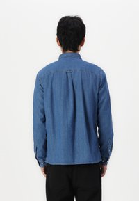 Men's denim shirt, dark blue, button-up design, long sleeves, pointed collar, yoke detail, and a straight hem. Fabric appears smooth.