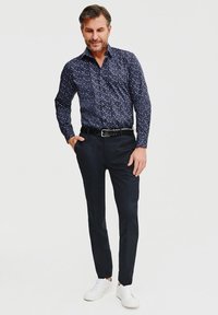 Granatowa koszula zapinana na guziki w biało-niebieski nakrapiany wzór, połączona z dopasowanymi ciemnymi spodniami i białymi trampkami. Wkładana do środka.