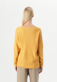 Maglione giallo a costine con scollatura ampia e spalle cadenti, caratterizzato da una vestibilità rilassata e un orlo posteriore leggermente più lungo.