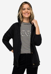 Cardigan nero a maglia grossa con cappuccio, presenta chiusura a bottoni e polsini a costine, indossato sopra una maglietta a righe con un design grafico.