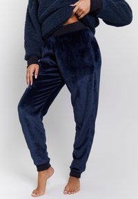 Pantaloni jogger in velour blu navy con vita e polsini elasticizzati, caratterizzati da una texture morbida e una vestibilità rilassata. Senza motivi visibili o accessori.