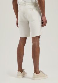 Helle beige Shorts mit einem elastischen Bund, ausgestattet mit Gesäßtaschen und subtiler Textur, kombiniert mit hellen Sneakers.