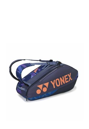 Bolsa deportiva Yonex azul marino con logo naranja, correas con patrones geométricos y compartimentos con cremalleras, diseñada para llevar raquetas y equipo.