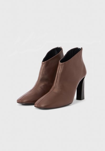 Bottes courtes en cuir marron avec un design à bout pointu, fermeture éclair à l'arrière et talon bloc, présentant une texture lisse et une silhouette épurée.