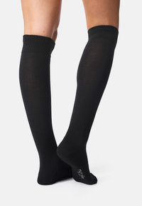 Calcetines negros hasta la rodilla con un puño acanalado, textura suave y un diseño ajustado. Presentan un logo en la planta.