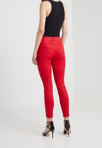 Rode slim-fit broek gemaakt van rekbare stof, met een gemiddelde taillehoogte, achterzakken en een gladde textuur. Gecombineerd met zwarte hoge hakken.
