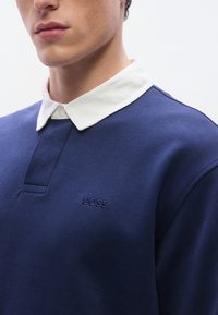 Μπλε ναυτικό πόλο φούτερ με λευκό γιακά, με διακριτικό κεντητό λογότυπο "BOSS" και πατιλέτα με κούμπωμα κουμπιού.