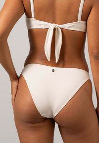 Vit bikiniöverdel med knytbakdetalj och matchande höga bikiniunderdelar. Tyget har en strukturerad yta och visar upp en elegant design.