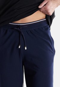 Navy blue sweatpants, featuring a drawstring waist with silver and white accents. Soft fabric with two side pockets and relaxed fit.