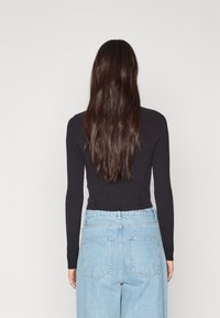 Sort ribbet langærmet bluse parret med høj talje lyseblå denimjeans, der har en bred benåbning og baglommer.