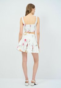 Weißes Blumen-Crop-Top und fließendes Rock-Set, mit einem Reißverschluss auf der Rückseite, Blumenmuster in Pink und Grün und einem strukturierten Stoff.