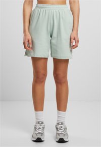 Light green cotton shorts with an elastic waistband, side slits at the hem, and a relaxed fit, paired with gray athletic shoes and white socks.