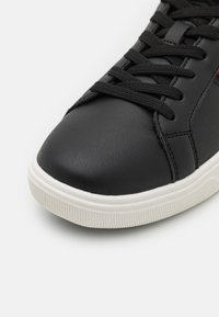 Schwarze Ledersneaker mit einer abgerundeten Spitze, strukturiertem Obermaterial und kontrastierender weißer Gummisohle. Ausgestattet mit schwarzen Schnürsenkeln und minimalen Nähten.