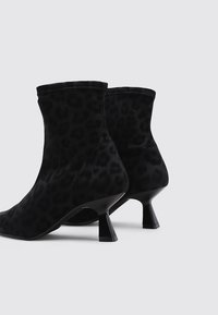 Botas negras hasta el tobillo con un diseño de estampado de leopardo. Fabricadas en un tejido suave, con un exclusivo tacón acampanado y una textura lisa.