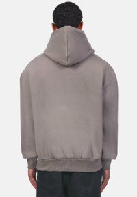 Graue oversized Kapuzenpullover mit einer großen Kapuze, gerippten Bündchen und Saum. Hergestellt aus weichem Material, mit glatter Textur und minimalen Nähdetails.
