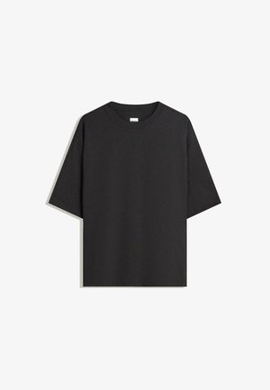 T-shirt noir à manches courtes, col rond, de coupe décontractée et légèrement oversize, posé à plat sur une surface blanche.