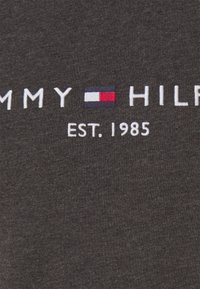 Šedé bavlněné tričko s bílým vyšívaným textem "TOMMY HILFIGER" a "EST. 1985" s modrým, červeným a bílým logem.
