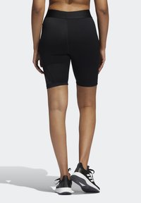 Shorts de sport noirs avec une coupe ajustée, une texture lisse et une large ceinture. Marquage minimal sur le côté inférieur gauche.