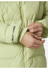 Světlý zelený nárazuvzdorný kabát se zipem vpředu, elastickými manžetami a logem "Helly Hansen" na rukávu. Hladká textura a prošívaný design.