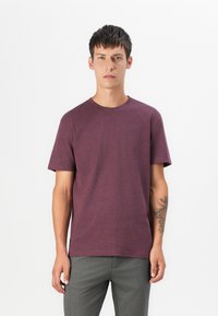 Bordeauxfarbenes T-Shirt mit kurzen Ärmeln aus strukturiertem Stoff. Rundhalsausschnitt und lässige Passform, kombiniert mit grauen Hosen. Keine auffälligen Muster oder Akzente.