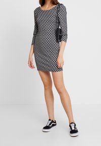 Czarna i biała wzorzysta sukienka z rękawami 3/4, dopasowany fason i boczną kieszenią. Połączona z czarnymi trampkami z białymi akcentami.