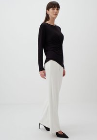 Zwarte lange mouwen top met een gedraaide design, gecombineerd met witte wijde broek. De outfit heeft een slanke silhoutte en zwarte puntige hakken.