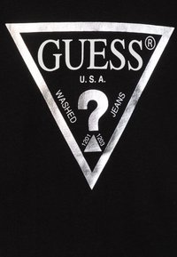 Black cotton t-shirt featuring a silver triangular logo with "GUESS," "WASHED," and a question mark, along with numeric details.