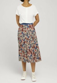 Haut blanc à manches courtes avec pli avant ; jupe midi plissée à fleurs dans les tons rouge, bleu et crème ; associée à des baskets blanches à lacets.