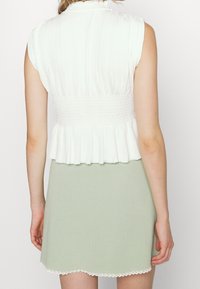 Weißes, geripptes Cropped-Top mit gerafftem Bund und Rüschensaum, kombiniert mit einem hellgrünen Rock mit gewelltem Saum und strukturiertem Stoff.